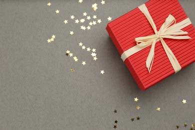 Red gift box and shiny confetti on grey background, top view. Space for text