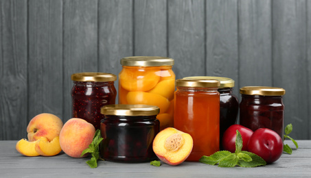 Glass jars with different pickled fruits and jams on grey wooden background