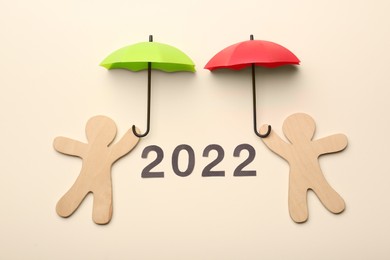 Mini umbrellas, figures of people and number 2022 on beige background, flat lay