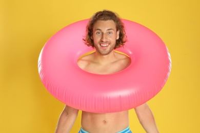Attractive young man in swimwear with pink inflatable ring on yellow background