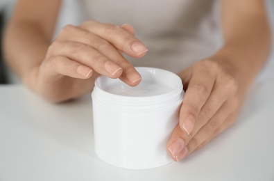 Woman with jar of moisturizing cream at white table, closeup