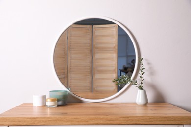 Trendy round mirror and chest of drawers near white wall. Interior element