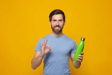 Photo of Man with green thermo bottle showing ok gesture on orange background. Space for text