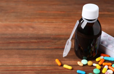 Photo of Bottle of syrup, dosing spoon and pills on wooden table, space for text. Cold medicine
