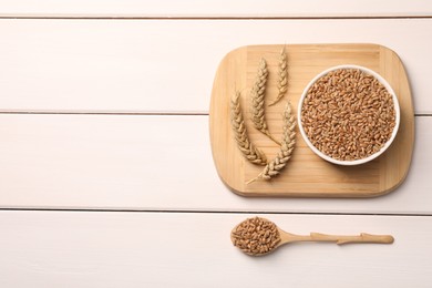 Photo of Wheat grains with spikelets on white wooden table, flat lay. Space for text