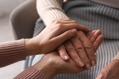 Young and elderly women holding hands together on blurred background, closeup