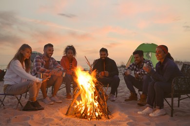 Friends sitting around bonfire on beach in evening