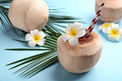 Fresh coconut with drinking straws and flowers on light blue background