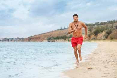 Handsome male lifeguard running on sandy beach