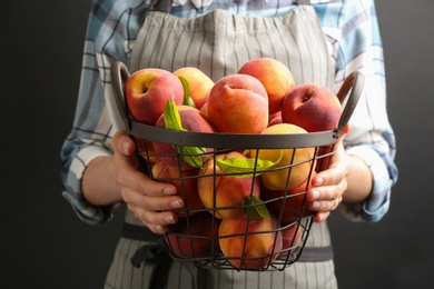 Woman with fresh sweet peaches in metal basket, closeup