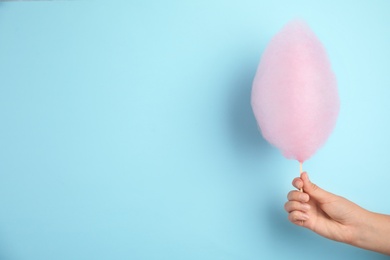Photo of Woman holding sweet pink cotton candy on light blue background, closeup view. Space for text