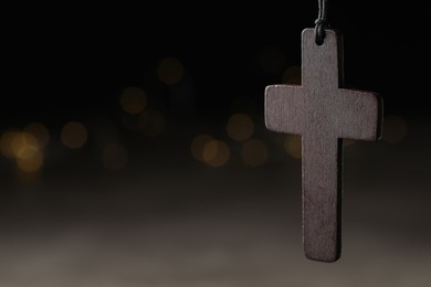 Wooden Christian cross against blurred lights, closeup. Space for text