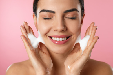 Photo of Young woman applying cosmetic product on pink background, closeup. Washing routine