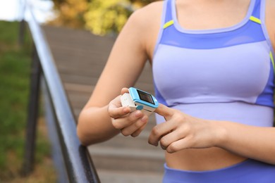 Woman checking pulse with blood pressure monitor on finger after training outdoors, closeup. Space for text
