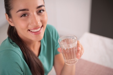 Young woman holding glass of pure water indoors, closeup