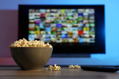 Bowl of popcorn and TV remote control on table indoors