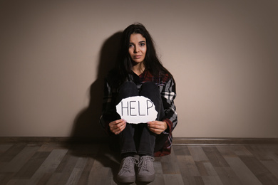 Photo of Abused young woman with sign HELP near beige wall. Domestic violence concept