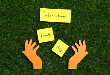 Photo of Cards with text International Family Day and paper hands on green grass, flat lay
