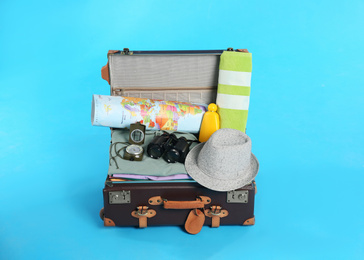 Open vintage suitcase with clothes packed for summer vacation on light blue background