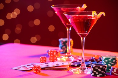 Cocktail, dice, playing cards and casino chips on table against blurred lights. Space for text