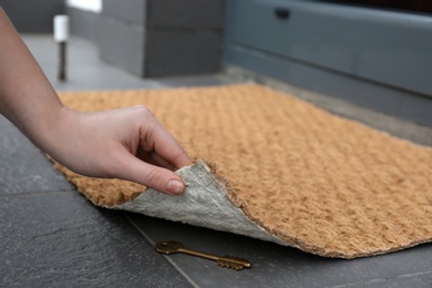 Photo of Woman lifting door mat to reveal key hidden underneath, closeup. Space for text