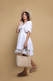Young woman with stylish bag and smartphone on beige background