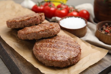 Serving board with tasty grilled hamburger patties on wooden table, closeup