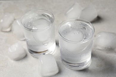 Shot glasses of vodka with ice cubes on light grey table, closeup