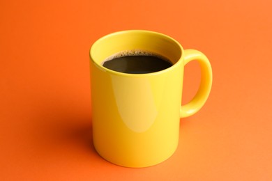 Yellow mug of freshly brewed hot coffee on orange background