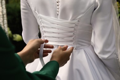 Woman helping bride to put on wedding dress outdoors, closeup