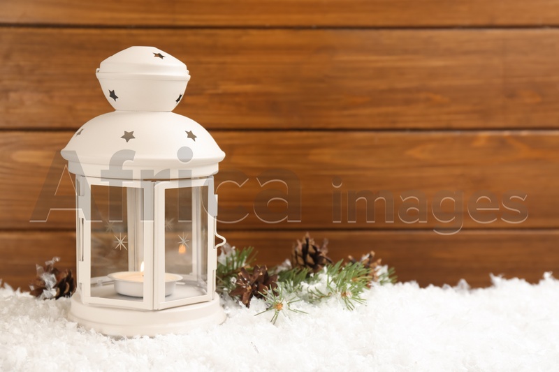 Photo of Christmas lantern with burning candle and fir tree branch on snow. Space for text