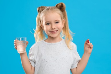 Little girl with vitamin pill and glass of water on blue background