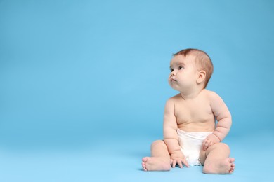 Cute little baby in diaper sitting on light blue background. Space for text