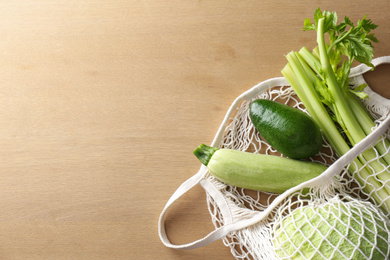 Different fresh vegetables in eco mesh bag on wooden table, top view