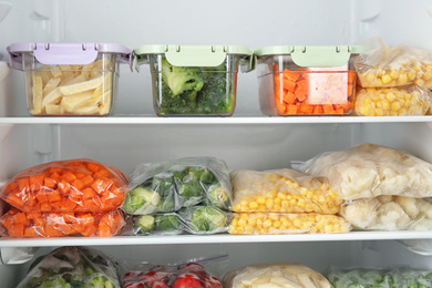 Plastic bags and containers with different frozen vegetables in refrigerator
