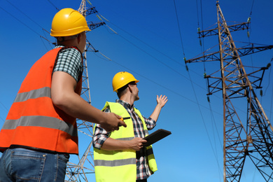 Professional electricians in uniforms near high voltage towers