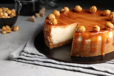 Photo of Sliced delicious cheesecake with caramel and popcorn on light grey table, closeup