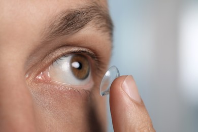 Man putting contact lens in his eye on blurred background, closeup