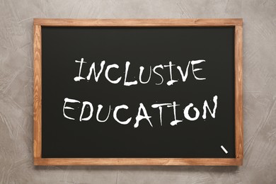Small blackboard with word INCLUSIVE EDUCATION on light grey stone background, top view