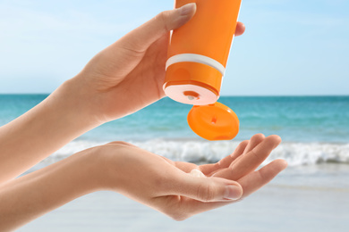 Young woman applying sun protection cream near sea, closeup