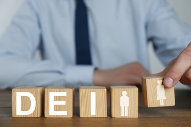 Concept of DEI - Diversity, Equality, Inclusion. Businessman and wooden cubes with letters and image of people on table, closeup