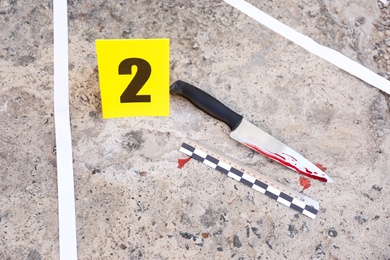 Photo of Crime scene with bloody knife and evidence mark on floor, above view. Detective investigation