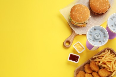 Different fast food on yellow background, flat lay. Space for text