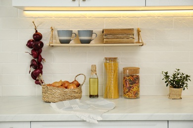 Fresh onions and other products on white countertop in modern kitchen