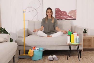 Young mother meditating on sofa in messy living room