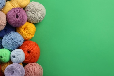 Soft woolen yarns on green background, flat lay. Space for text