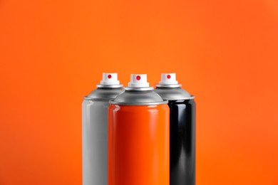 Colorful cans of spray paints on orange background, closeup