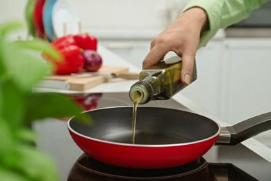 Photo of Woman pouring cooking oil from bottle into frying pan in kitchen, closeup