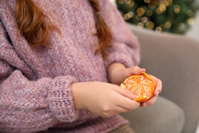 Little girl peeling fresh tangerine on sofa at home, closeup