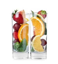 Glasses with different whole and cut fruits on white background